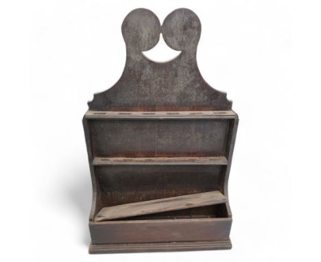 An 18th century provincial oak spoon rack, the scroll carved pediment over two six-hole racks, with candlestick compartment t