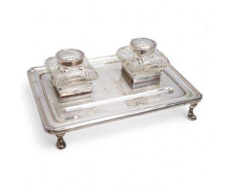 George V silver inkstand of rectangular design with pen tray and two cushion shape glass inkwells with silver covers, raised 