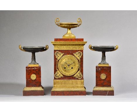 A French empire style ormolu mounted rouge marble mantel clock garniture C.1860, with urn surmount over a rectangular body en