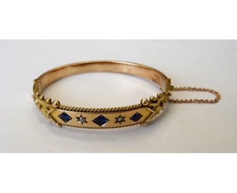 A 9ct gold, sapphire and diamond set oval hinged bangle, mounted with three cushion shaped sapphires and with two rose diamon