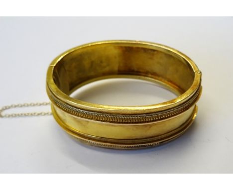 A Victorian gold oval hinged bangle, the front with applied decoration in the classical taste, on a snap clasp, detailed 15 C