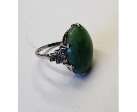 A platinum, jade and diamond ring, claw set with the oval jade cabochon between diamond set stepped shoulders in the Art Deco