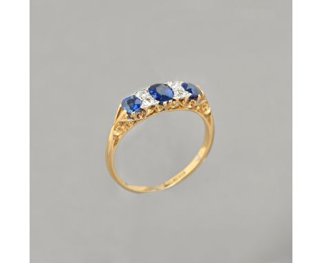 A gold and platinum, sapphire and diamond ring, mounted with three oval cut sapphires and with two pairs of cushion shaped di