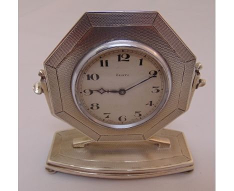 A hallmarked silver mounted eight day desk clock, octagonal engine turned, the shaped rectangular base on four bun feet, Birm