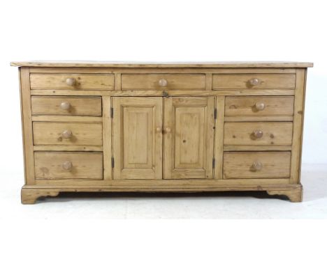 A pine sideboard, 20th century, with nine drawers and central cupboard with single shelf, turned handles and bracket feet, 16