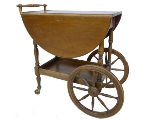 A mid 20th century mahogany and stained beech drinks trolley, with oval drop leaf surface, turned handle, lower shelf and car