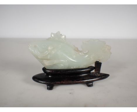 A Chinese celadon Jade carved Fish with lily pad and flower to one side, small chips, on hardwood stand, approx 3 3/4in long