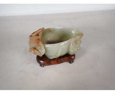 An Oriental jade lotus blossom Bowl with carved leafage design on a hardwood stand, 4 in long