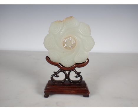 A Chinese celadon Jade Bi Disk carved flower head with geometric carved centre section on hardwood stand, approx 3in diameter