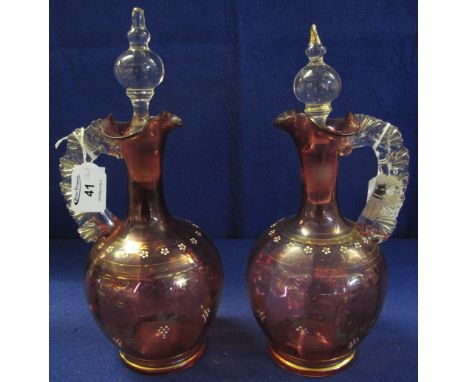 Pair of cranberry glass ewers with clear shell moulded loop handles, over-gilded and enamel floral decoration and similar but