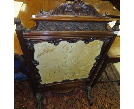 A Victorian mahogany firescreen, the heavy carved decoration and central needlework panel depicting birds and flowers 