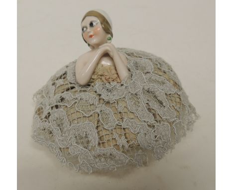 An Art Deco ceramic half doll powder puff, the doll with white cap, sideways glancing googly eyes and with hands clasped unde