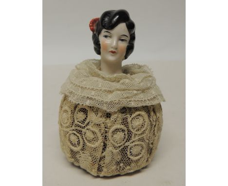 A 1920's lazed porcelain head pin cushion, the head of a young woman with black flapper style hair dressed with red comb and 