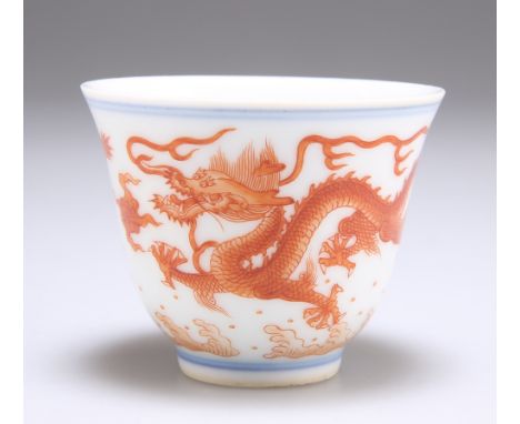 A CHINESE PORCELAIN WINE CUP, the tapering bowl iron red painted with five-claw dragons between paired blue bands, bears iron