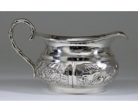 A Chinese Silvery Metal Oval Cream Jug, the bulbous body chased and embossed with four panels of animals, flowers, blossoms a