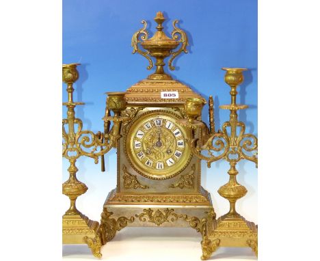 A BRASS CLOCK GARNITURE, THE TWO HANDLED CASE OF THE CLOCK SURMOUNTED BY AN URN, THE MOVEMENT STRIKING ON A BELL.   H 41cms. 