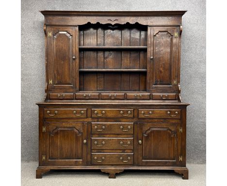 A 20th century Georgian style oak dresser having a moulded cornice with a shaped apron above two central shelves flanked by p