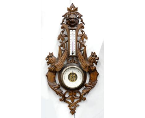 A FRENCH CARVED AND STAINED SOFTWOOD ANEROID BAROMETER, WITH LION MASK AND WINGED GROTESQUES, THE STEM INSET WITH AN ENAMEL A