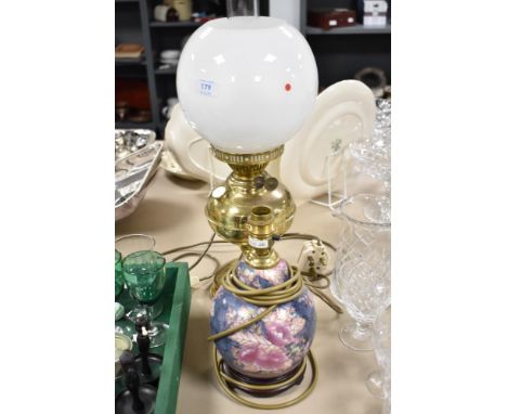 A brass table lamp in the form of an oil lamp and ceramic lamp base with floral decoration.