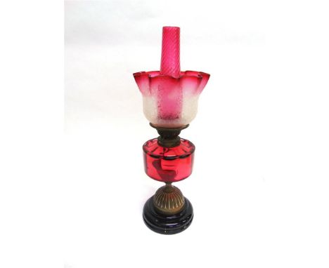 A VICTORIAN OIL LAMP with cranberry glass reservoir, funnel and shade, 56.5cm high