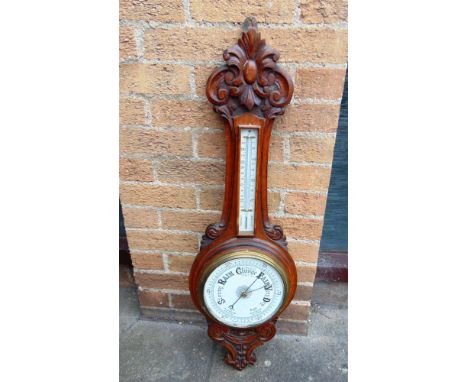 AN EDWARDIAN CARVED OAK ANEROID BAROMETER/THERMOMETER  the ceramic dial 20cm diameter, 90cm high overall