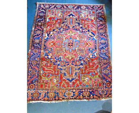 A HERIZ CARPET the red field with large angular medallion, within blue border wtih flowerhead and leaf design, 351cm x 254cm