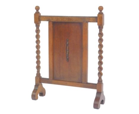 A 1920s oak firescreen, with spiral twist columns and a central panelled section, the scroll feet 67cm high, 50cm wide.