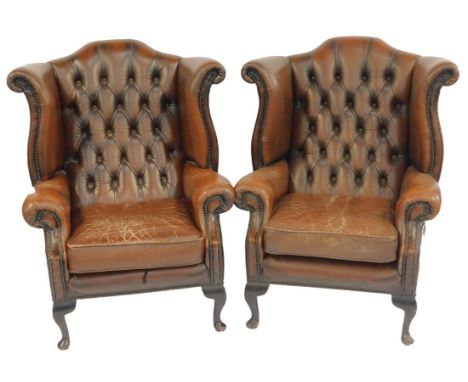 A pair of brown leather wing back armchairs, with button back, stud work and moveable seat, on mahogany pad feet. The upholst