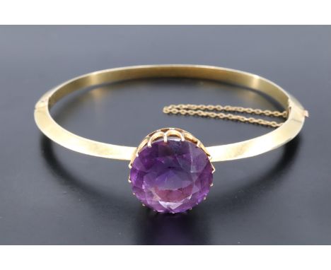 An impressive late 19th / early 20th Century amethyst and high carat yellow metal hinged bangle, the round cut stone of appro