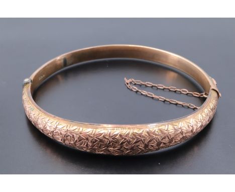 An early 20th Century 9 ct yellow metal hinged bangle, of D-section and decorated with foliate brightwork, 57 mm x 48 mm inte