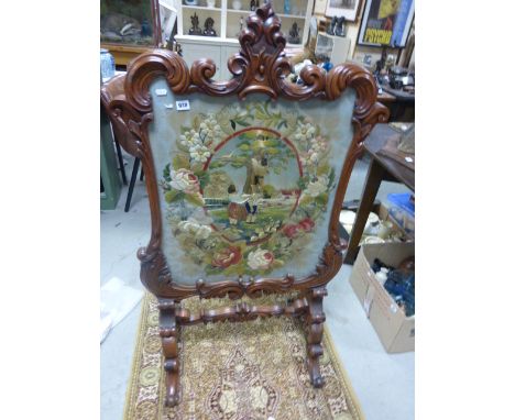 Large mahogany firescreen with ornate scroll carved frame inset with a glazed silk embroidery depicting three children playin