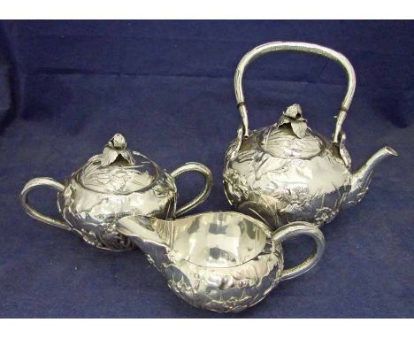 A Chinese export silver metal three-piece tea service of compressed circular form, each piece embossed with flowering lilies,