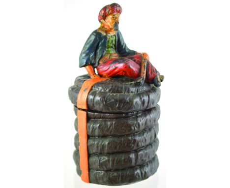 SNAKE CHARMER TOBACCO JAR. 8.5ins tall to top of lid. Ceramic seated snake charmer, base forms basket in brown, red & orange 