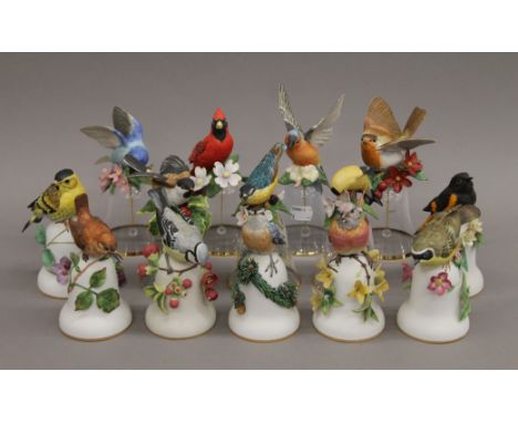 A quantity of various ceramic and glass bells decorated with bird form handles. The largest 18 cm high. 