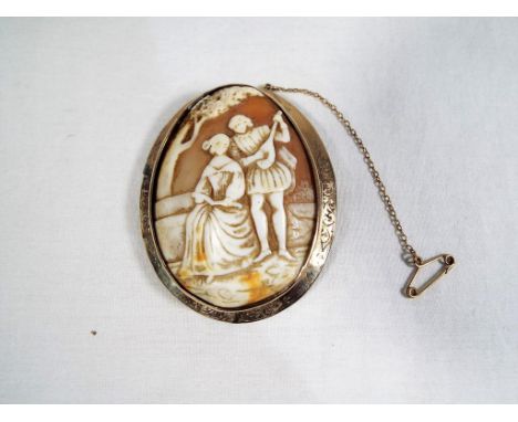 A cameo depicting a couple in period attire, she seated beneath a tree, he playing a lute, the yellow metal mount presumed 9 