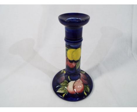 Moorcroft Pottery - a candlestick decorated with wisteria (plums) on a cobalt blue ground, signed to the base, 18 cm (high) -