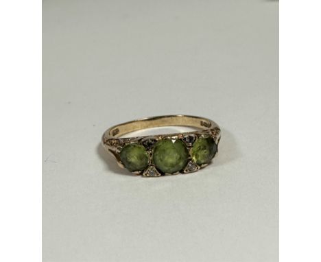 A 9ct gold peridot three stone ring with diamond set spacers, the centre stone approximately 0.5ct, flanked by approx 0.25ct,