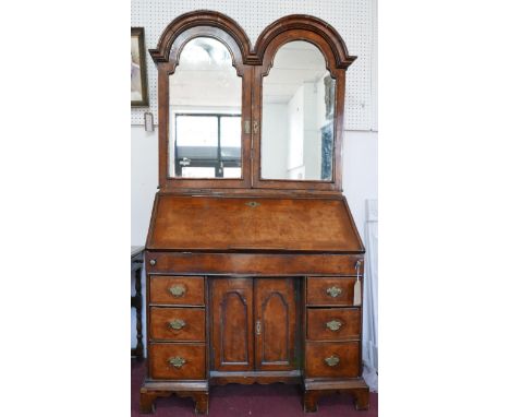 An early 18th century walnut bureau bookcase, the two arched mirrored doors enclosing drawers and shelf space, drop flap encl