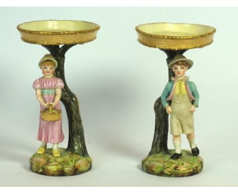 A pair of Royal Worcester hand painted figures
Modelled as a boy and a girl beside tree trunk supporting an oval bowl, raised