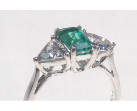 A fine quality 18ct white gold emerald and diamond set three stone ring
The central step cut emerald with a trillion cut diam