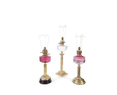 A COLLECTION OF THREE BRASS RESEVOIR LAMPS, including a clear glass and cranberry example, each converted to electricity. 64c