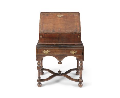 A GEORGE I WALNUT AND CROSSBANDED SLOPEFRONT BUREAU ON STAND, with engraved brass escutcheons and bracket handle, the fall fr