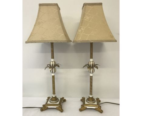 A pair of gold and white column style table lamps.  Each lamp has ball and leaf detail to middle of column on a square 4 foot