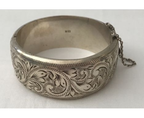 A vintage silver bangle with floral engraved detail and safety chain.  Engraving to one half. Hallmarked Birmingham 1973.  To