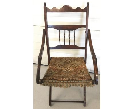 A vintage folding dark wood chair with carpet seat and spindle decoration to back.  