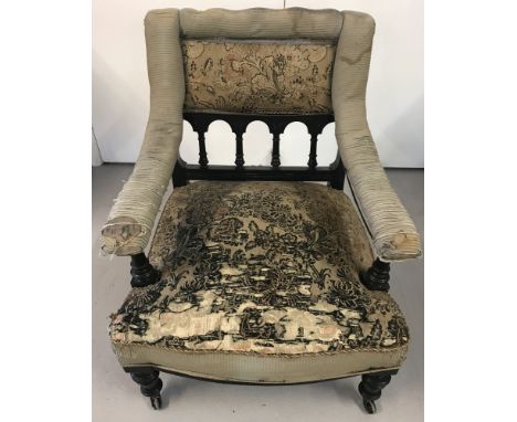 A Victorian ebonised and upholstered armchair on ceramic castors.  Turned detail to legs, arm rest supports and spindled back