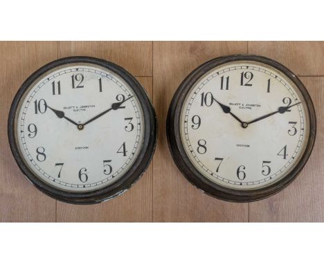 Two Gillett &amp; Johnston electric wall clocks, the cases in bronzed tin with Arabic numerals to the dial, 29cm diameter, wi