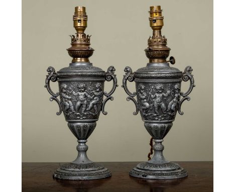 A pair of continental spelter oil lamps of vase form, decorated with putti, later converted for electric use, 36cm high overa