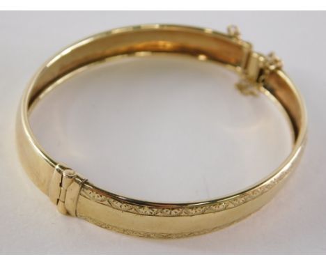 A 9ct gold hinged bangle, of half inch design with engraved borders, clasp and safety chain, 6cm diameter, yellow metal unmar