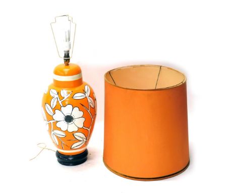 An orange retro pottery table lamp, with fixed top, vibrantly decorated with flowers, on a white and black ground, 80cm high.